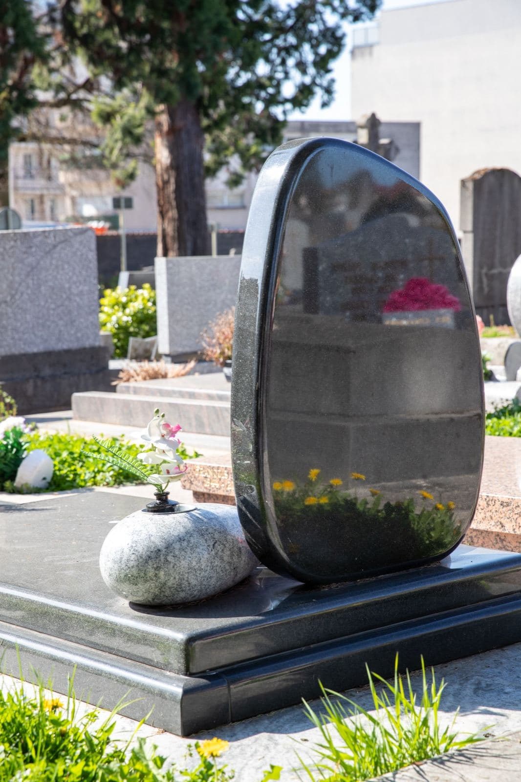 Stèle funéraire galet en granit poli sur une tombe fleurie
